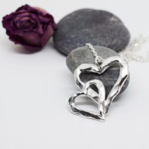 silverhalsband i forma av ett dubbelhjärta på stena med ros bakom