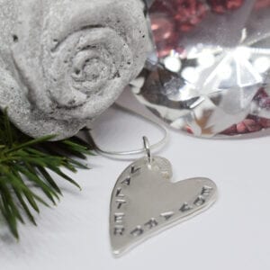 silverhjärta med text med betongros, grankvist och en diamant bredvid