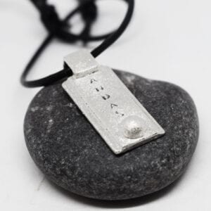 silversmycke med texten ANDAS på grå sten