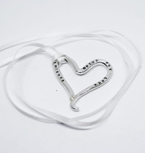 silverhjärta med text i vitt band på vit botten