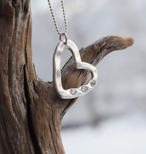 silverhjärta med stenar i kedja på träbit utomhus