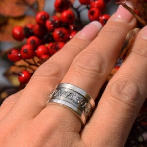 ring i silver på finger utomhus med rönnbär i bakgrunden