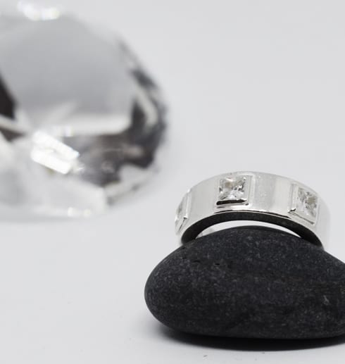 silverring med stenar på en svart sten och en stor diamant i bakgrunden