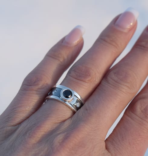 silverring med stor svart sten och mindre vita stenar på svartoxiderad botten på finger utomhus