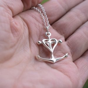silversmycke i form av kors, ankare och hjärta i handflata utomhus