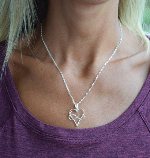 silverhalsband i form av ett hjärta med med en evighetssymbol på kvinna med lila tröja
