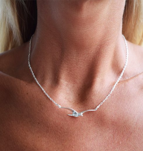 kvinnas hals med ett silverhalsband i form av en fiskmås