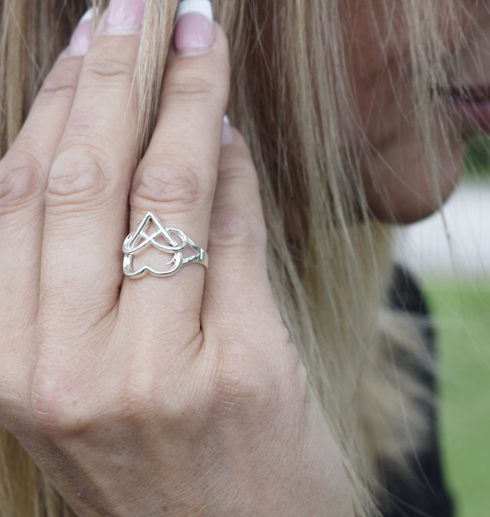 silverring med hjärta och evighetssymbol på kvinnas finger utomhus