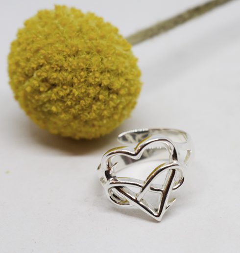 silverring med hjärta och evighetssymbol på vit botten med gul bollblomma