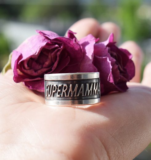 silverring med texten SUPERMAMMA med rosor bakom i hand utomhus