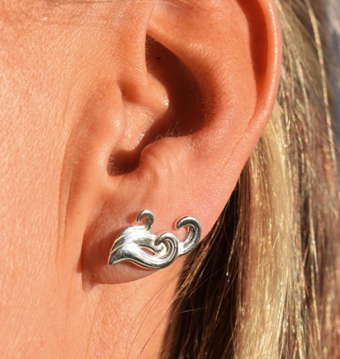 silverörhänge i form av vågor på kvinnas öra utomhus i solen