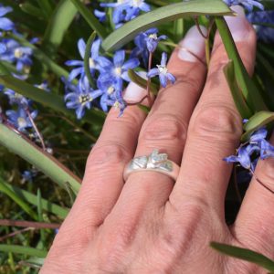 silverring med två hjärtan på kvinnas hand utomhus med blå blommor runt om