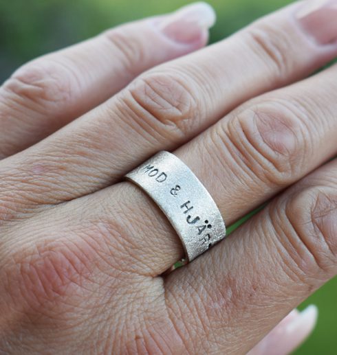 bred silverring med text på kvinnas finger utomhus