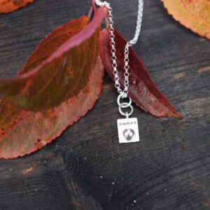 silverhalsband med texten ANDAS med orane löv bredvid
