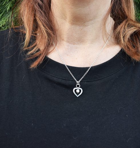 silverhalsband i form av ett hjärta runt kvinnas hals i svart tröja